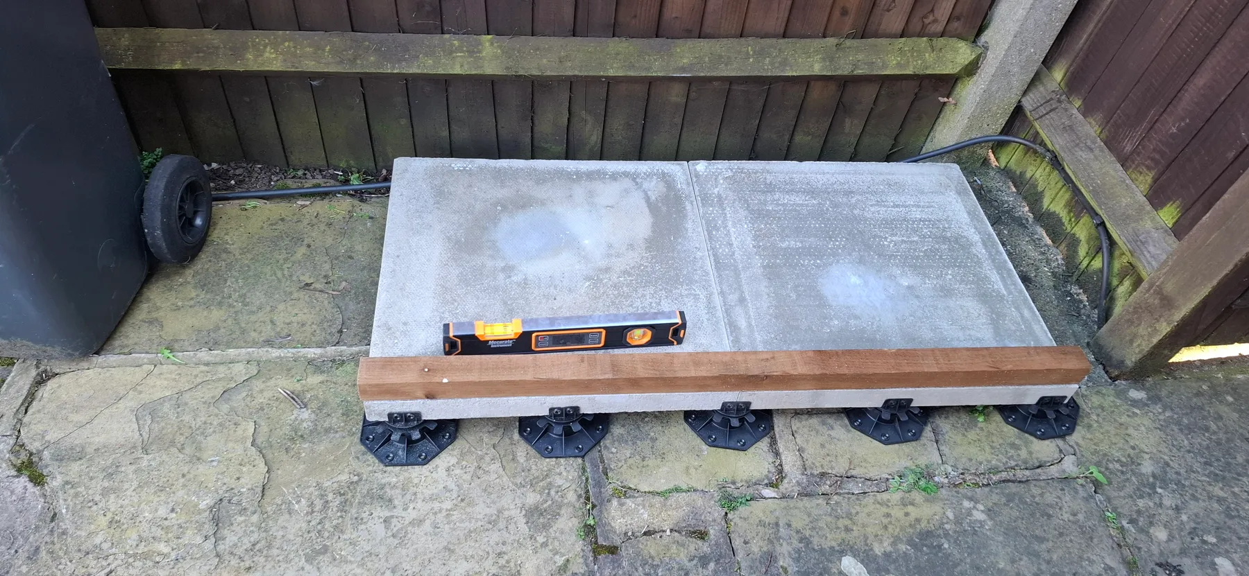 Paving slabs set on adjustable pedestals, with a spirit level and the first base timber in place