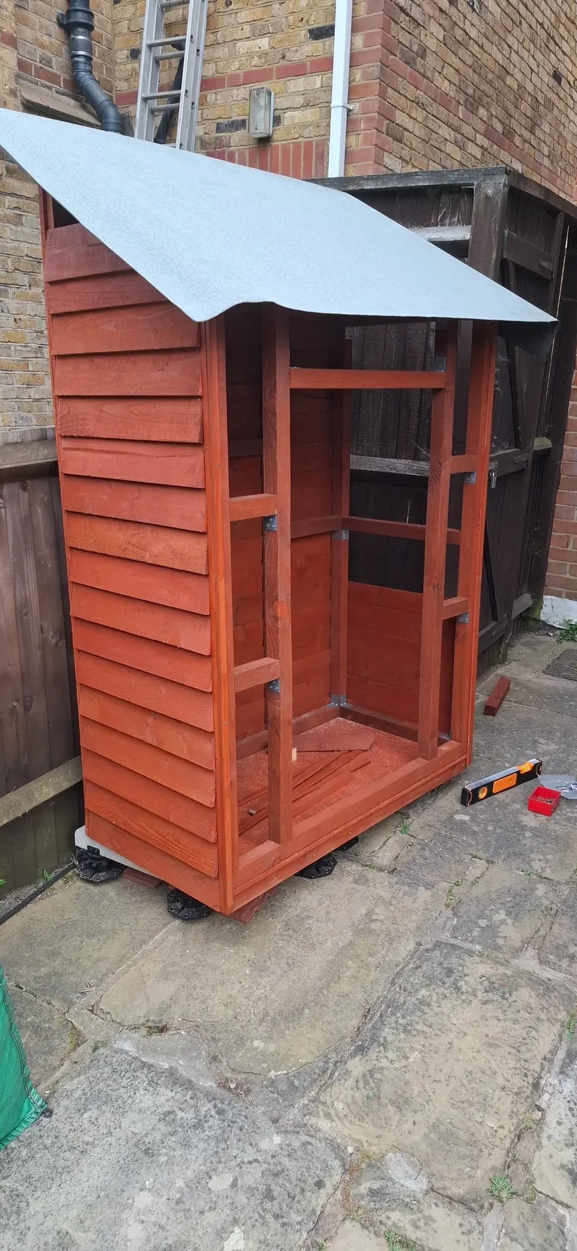 The shed frame standing upright, felt roof on, tools and offcuts scattered around it